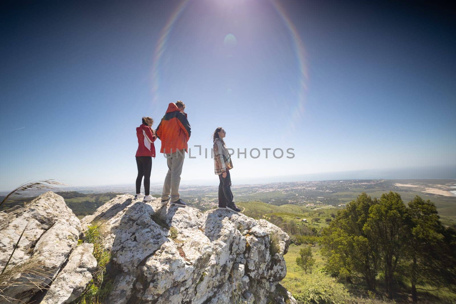 A group of friends is standing on a large rock formation, looking out at the landscape. They are enjoying the view and taking photos of the scenery.