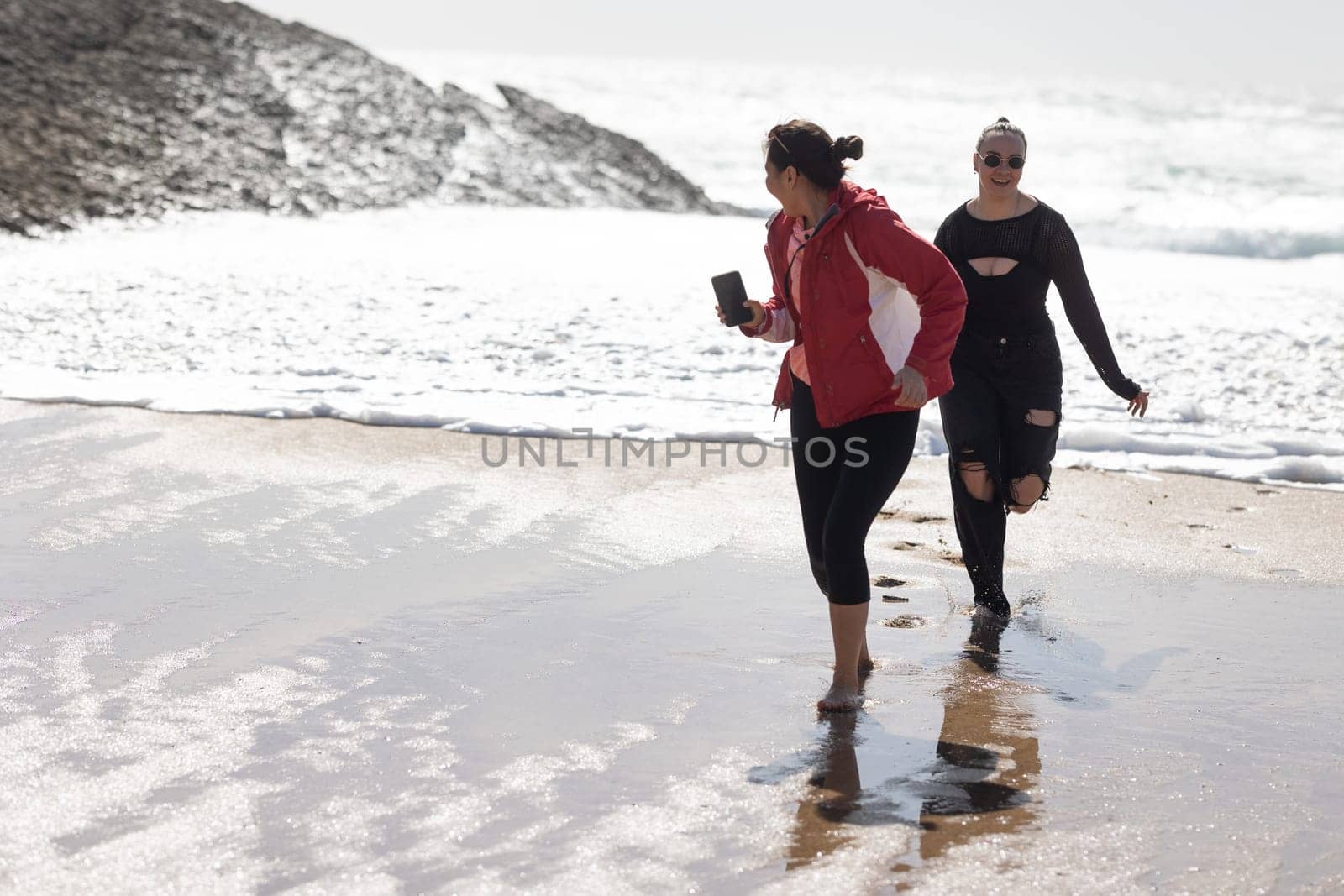 Two Women Walking Along Beach Next to Ocean by Studia72
