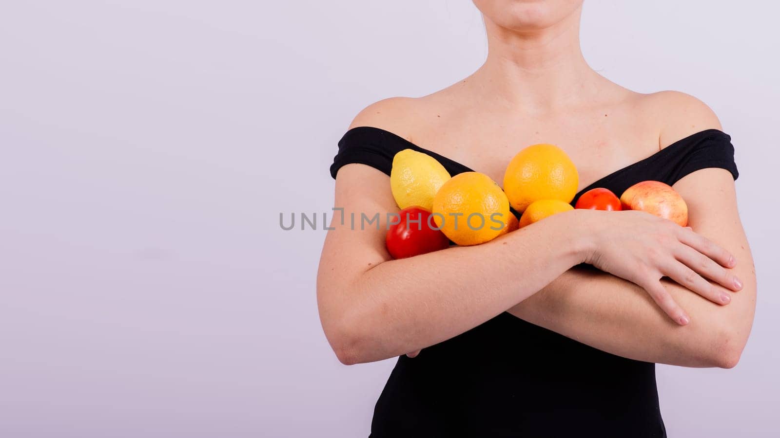 A female holding apples, lemons, oranges in different arms isolated on grey background. by Zelenin
