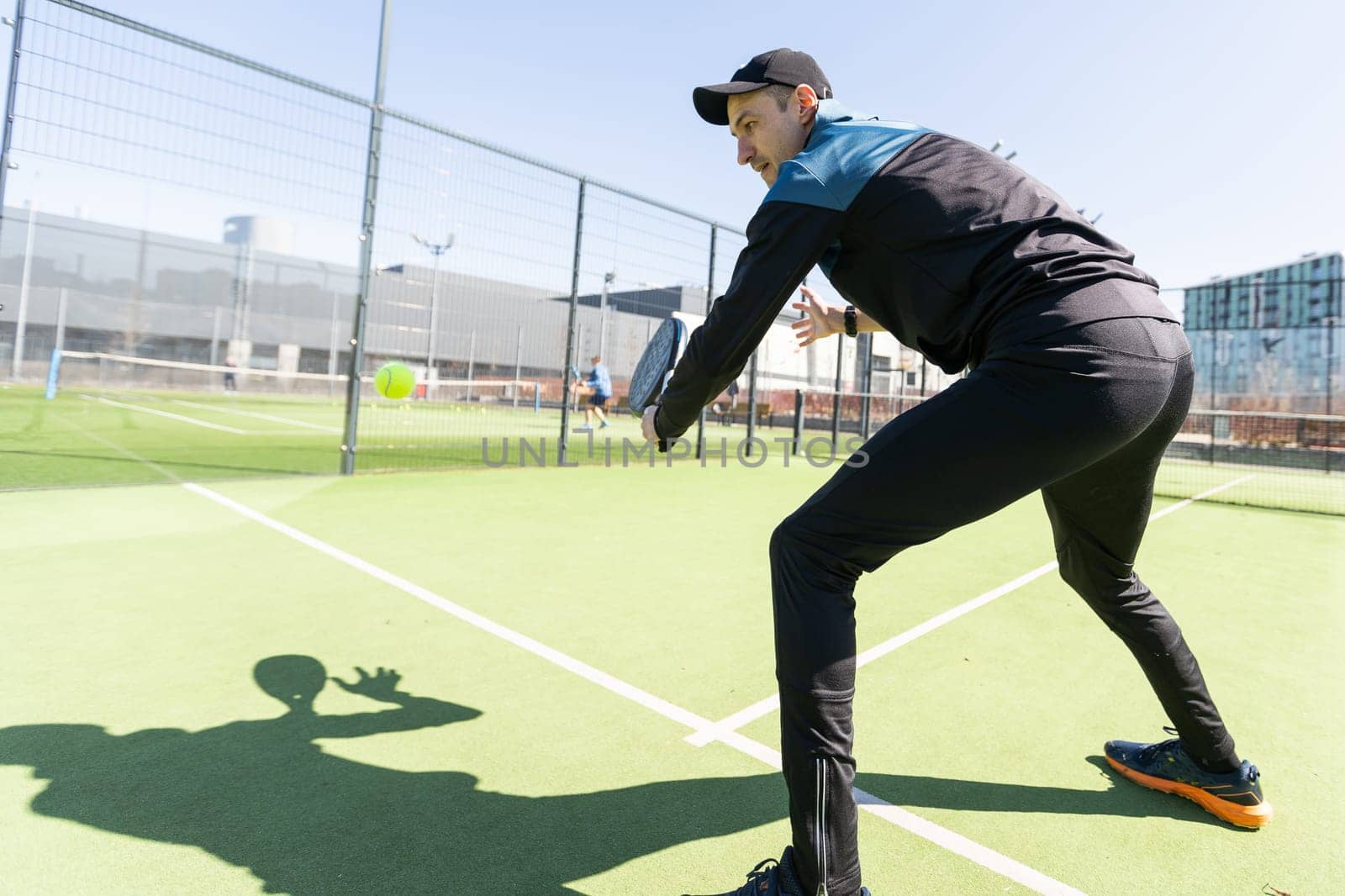 A padel player jump to the ball, good looking for posts and poster. Man with black racket playing a match in the open behind the net court outdoors. Professional sport concept with space for text by Andelov13