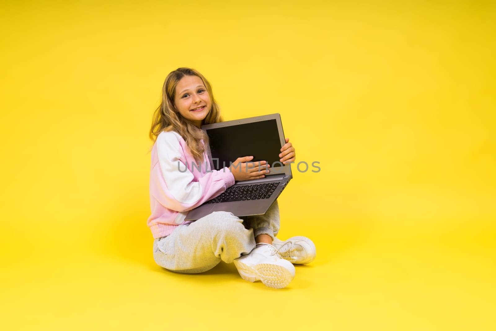 Positive kid sit with a laptop read homework wear casual style cloth isolated over yellow background
