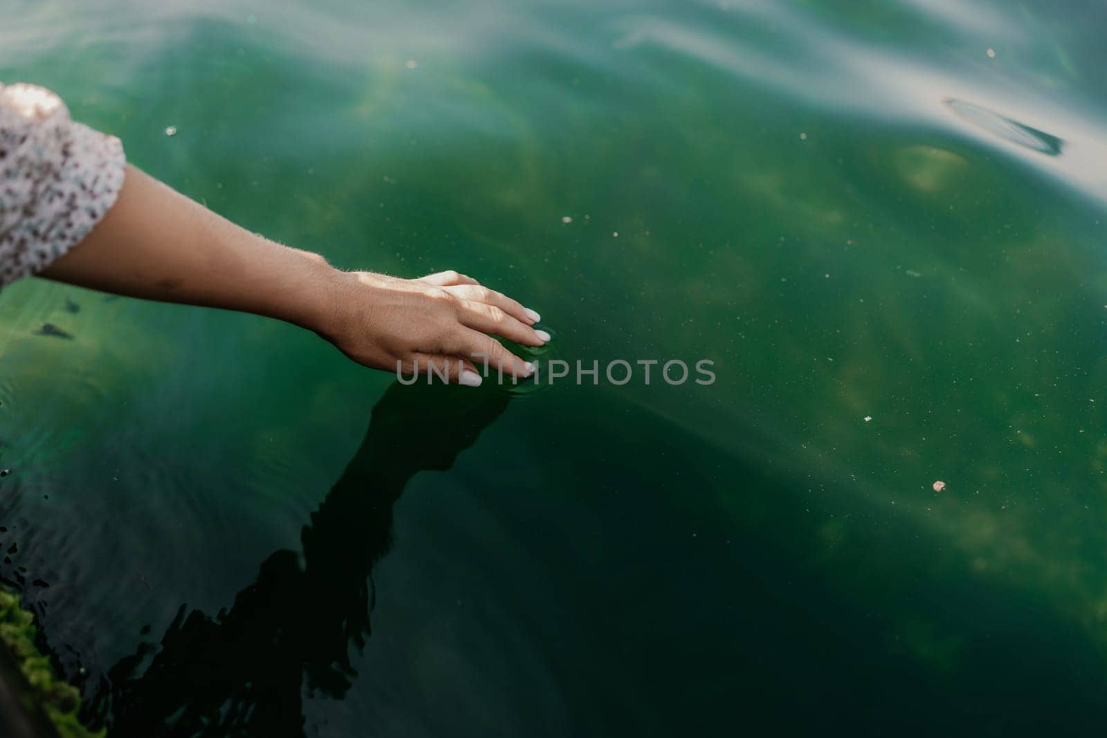 The hand touches the water, creating ripples. The water is calm and clear, and the hand is white. Concept of tranquility and peacefulness. by Matiunina