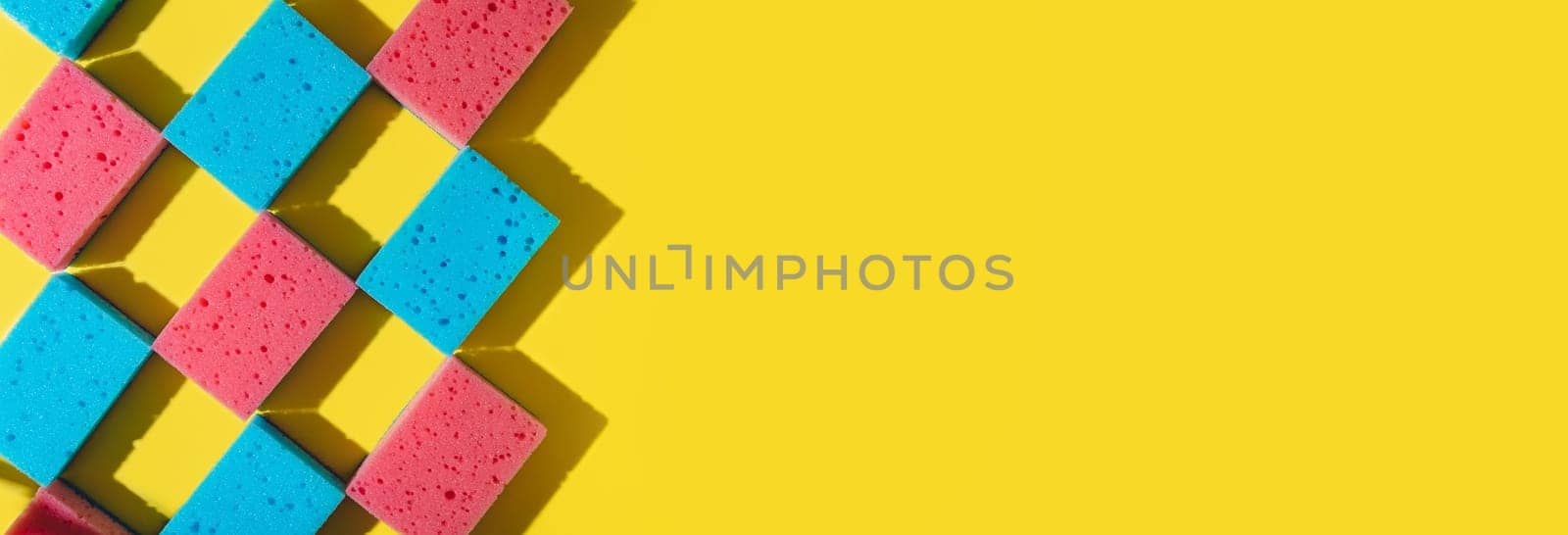 House cleaning sponges on yellow background, copy space. Flat lay or top view. Cleaning service or housekeeping concept with space. Hard shadows in sunlight. Long horizontal banner