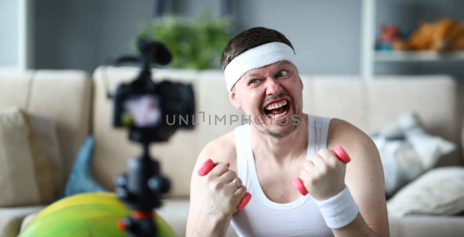 Blogger Holding Dumbbell in Hands for Exercise. Man with Funny Face Practice Fitness in Apartment. Male Recording Fitness Training on Digital Camera for Sport Blog. Bearded Sportsman Lifestyle