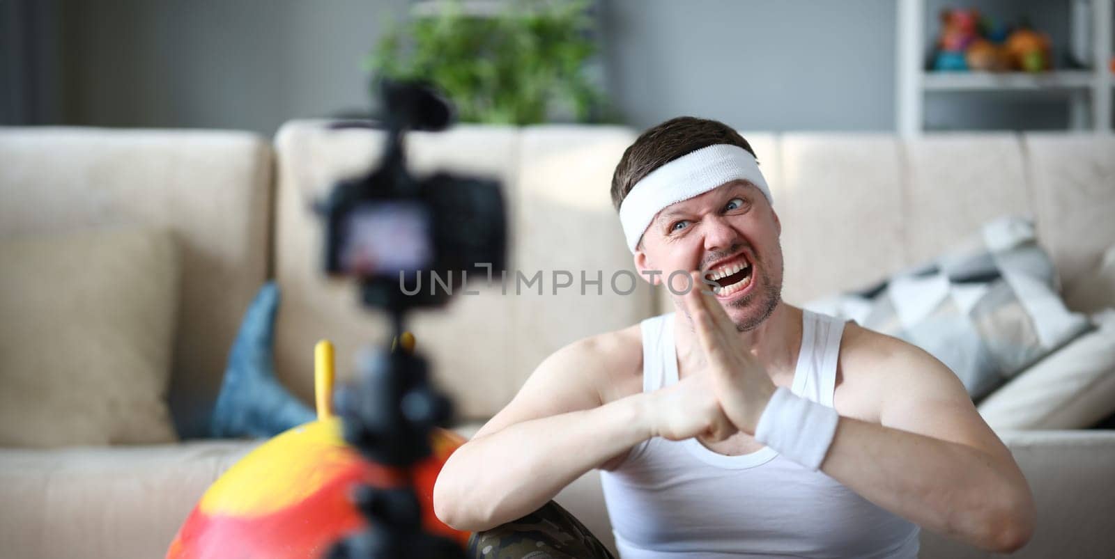 Blogger with Funny Face Record Fitness Exercise. Man Sportsman Shooting Workout on Digital Camera for Aerobic Blog. Bearded Male Training in Apartment. Guy Practice Healthy Lifestyle Photography