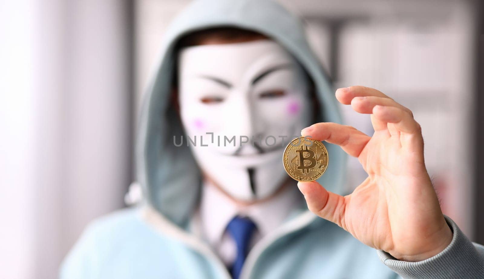 Tbilisi, Georgia, June, 2023: Hacker wear anonymus mask hold bitcoin in hand Illustrative editorial