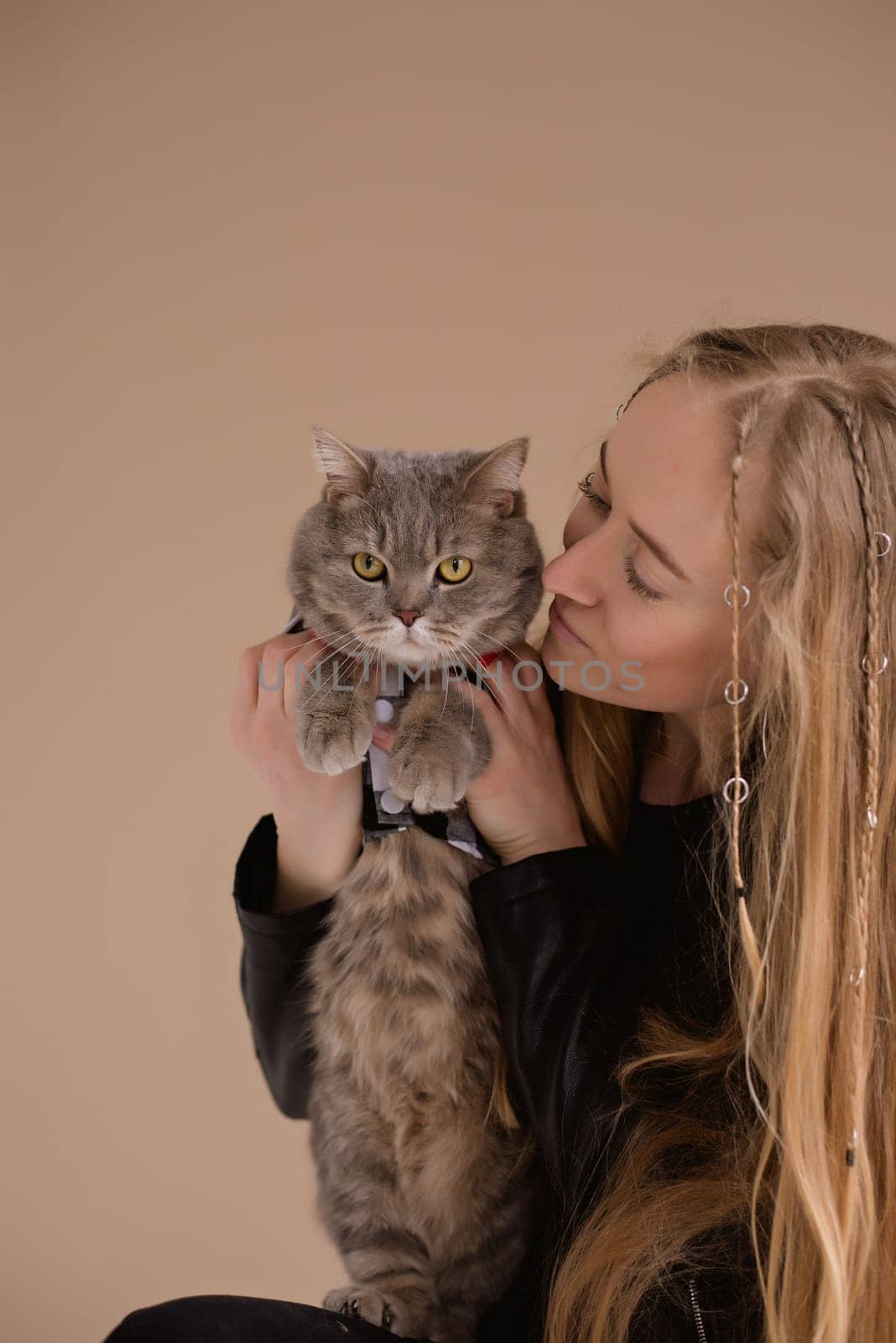 A woman natural blonde long hair smiling in a black clothes stand, sitting on photo studio. girl with pet scottish straight cat. portrait , vertical, close up