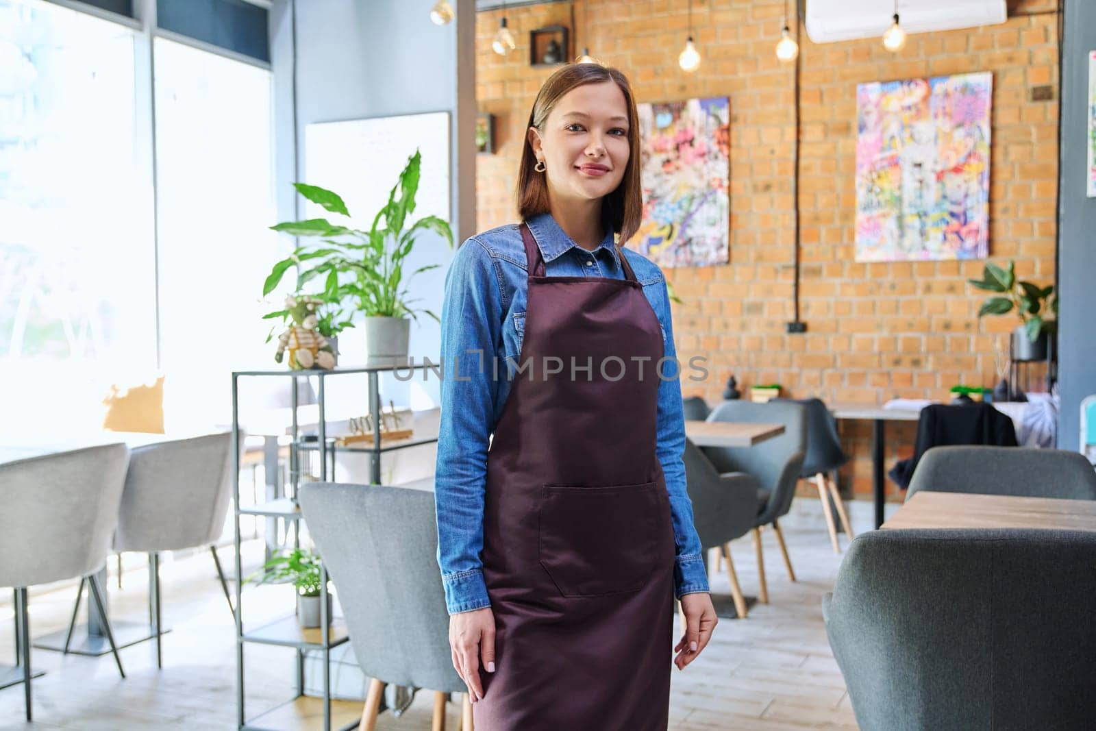 Attractive successful young woman service worker, business owner in apron looking at camera in restaurant cafeteria coffee pastry shop interior. Small business staff occupation entrepreneur work