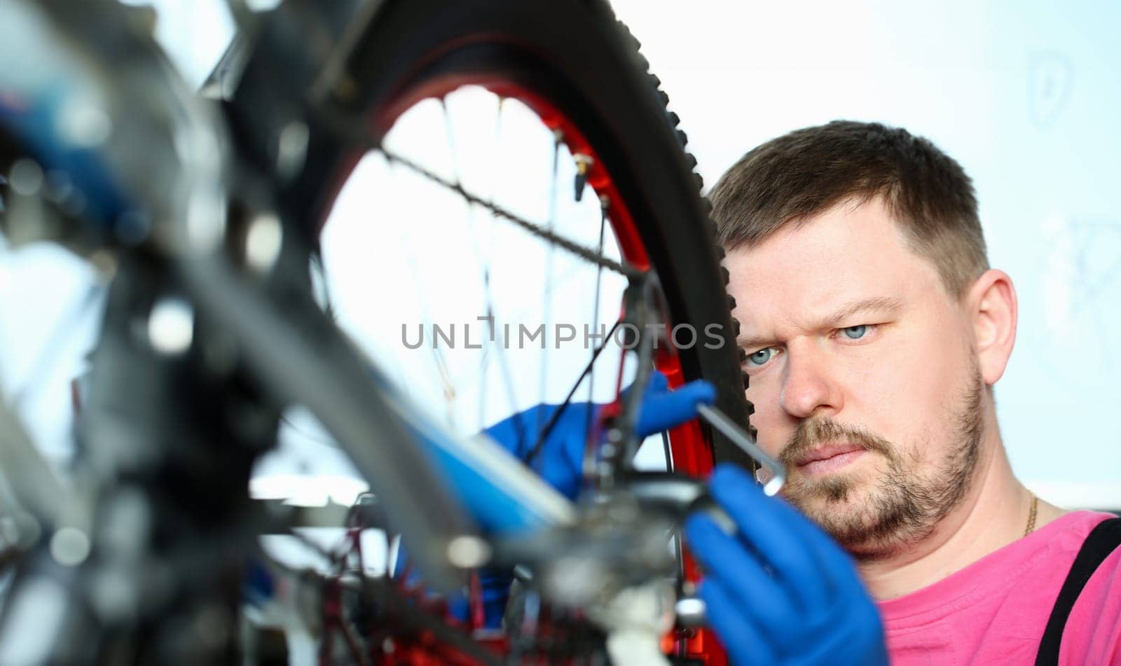 Male millennial repair man bicycle service in blue protective gloves adjusts bike to prepare for the season concept portrait