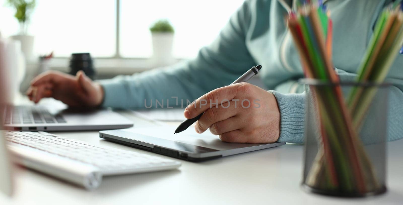 A young designer holds pen from tablet in hand working on new project for customer in field of building construction projects.