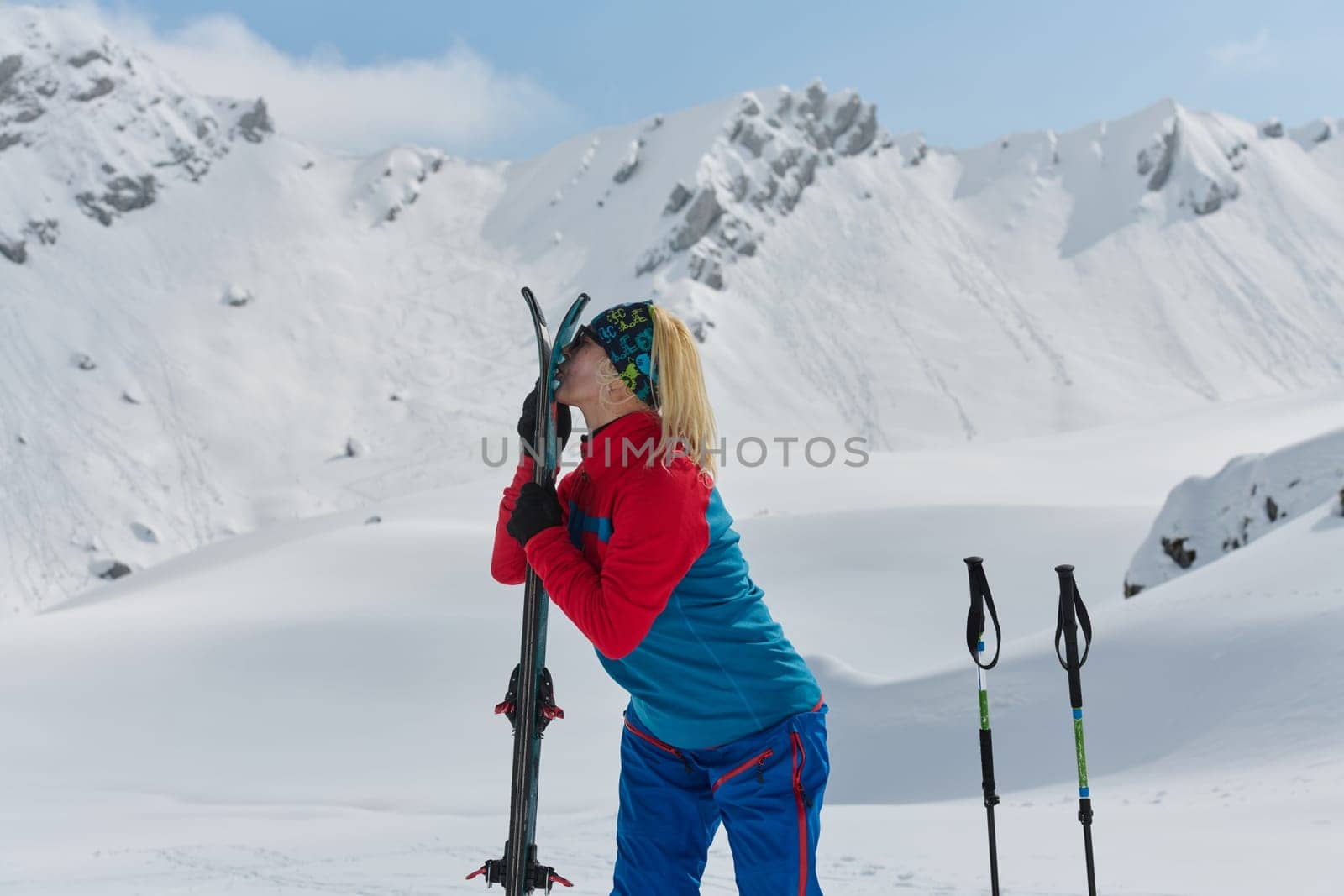 A Professional Female Skier Celebrates Success by Symbolically Licking Her Skis atop the Snowy Alps by dotshock