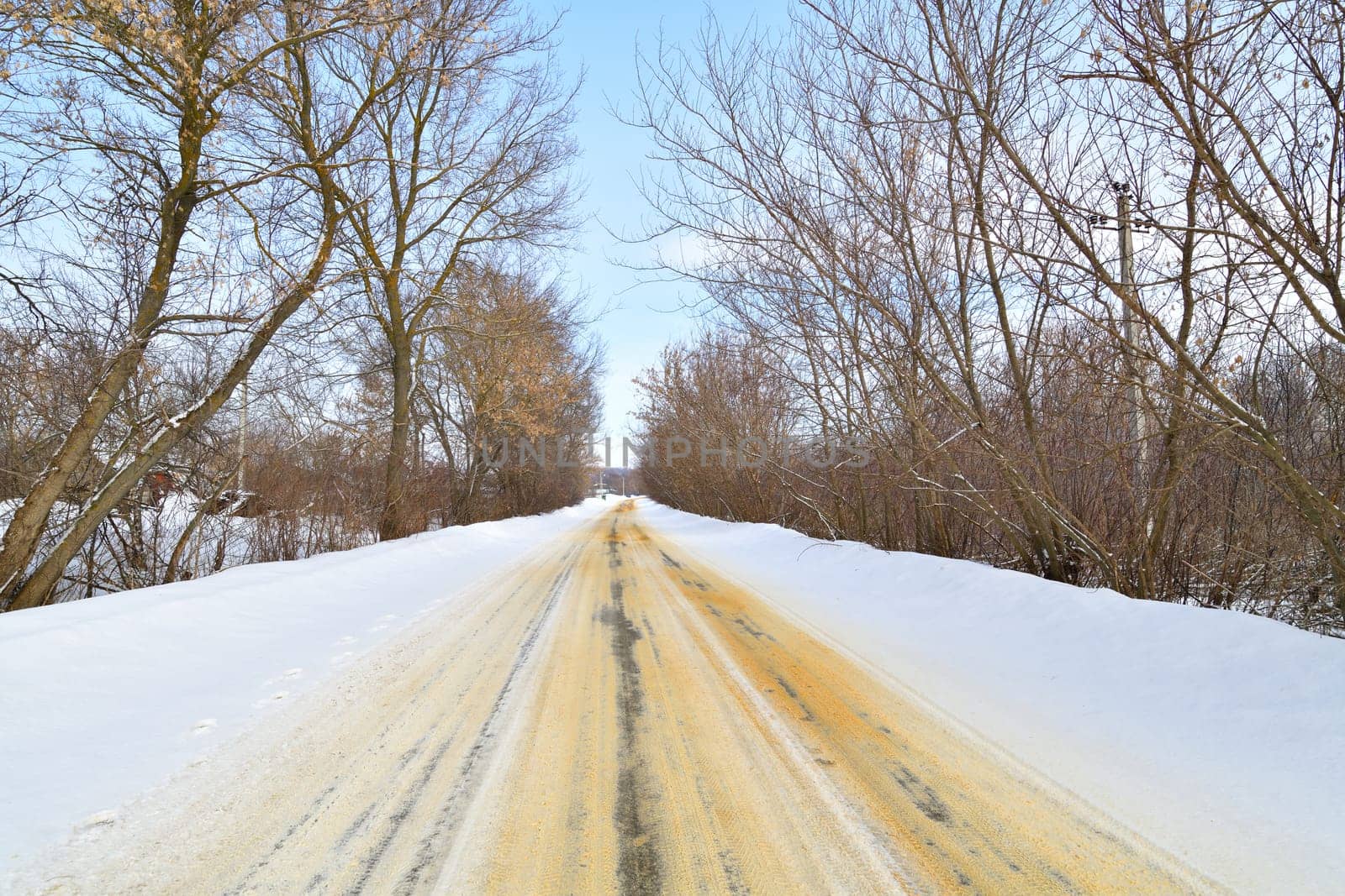 Rural winter road sprinkled with sand against ice by olgavolodina