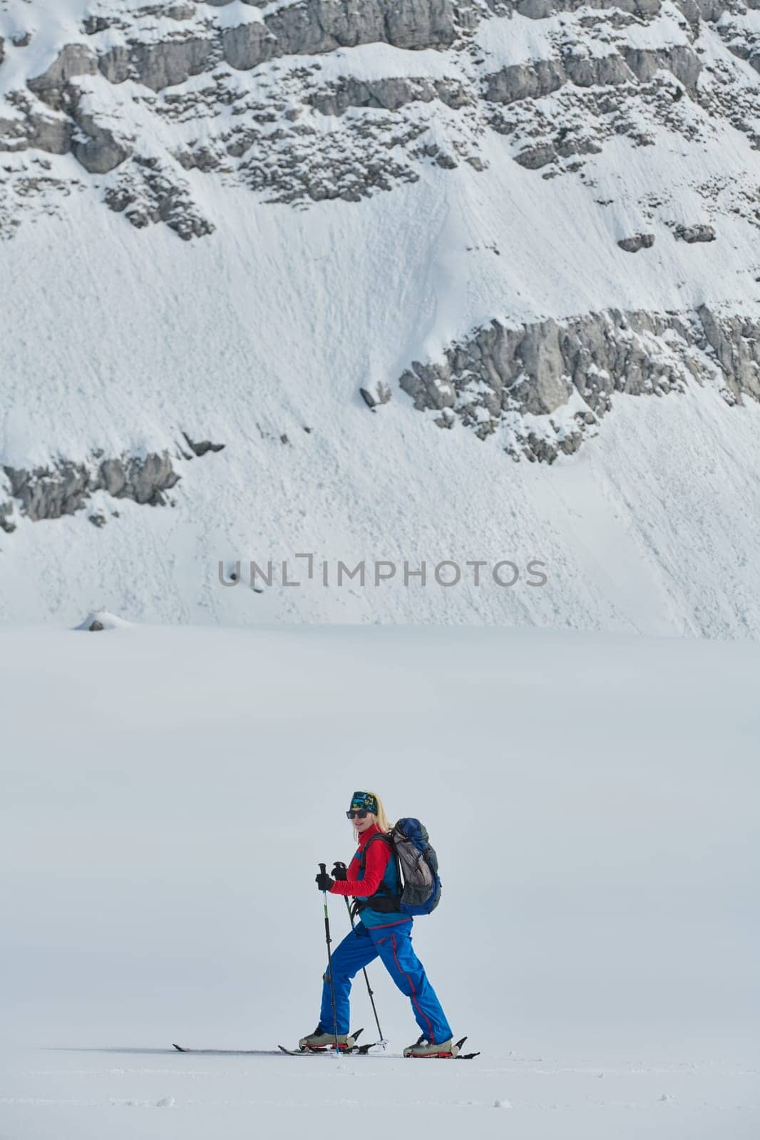 A female skier stands at the snowy summit of a mountain, equipped with professional gear and skis, poised for an exhilarating descent. by dotshock