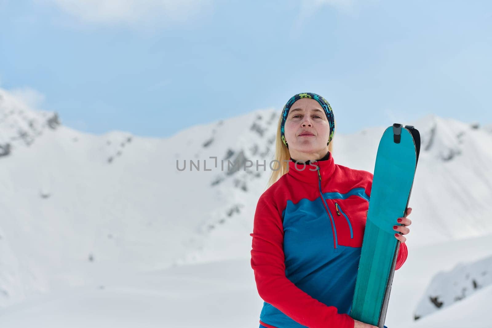 A triumphant female skier beams with confidence atop a snow-capped peak after conquering a challenging ascent.