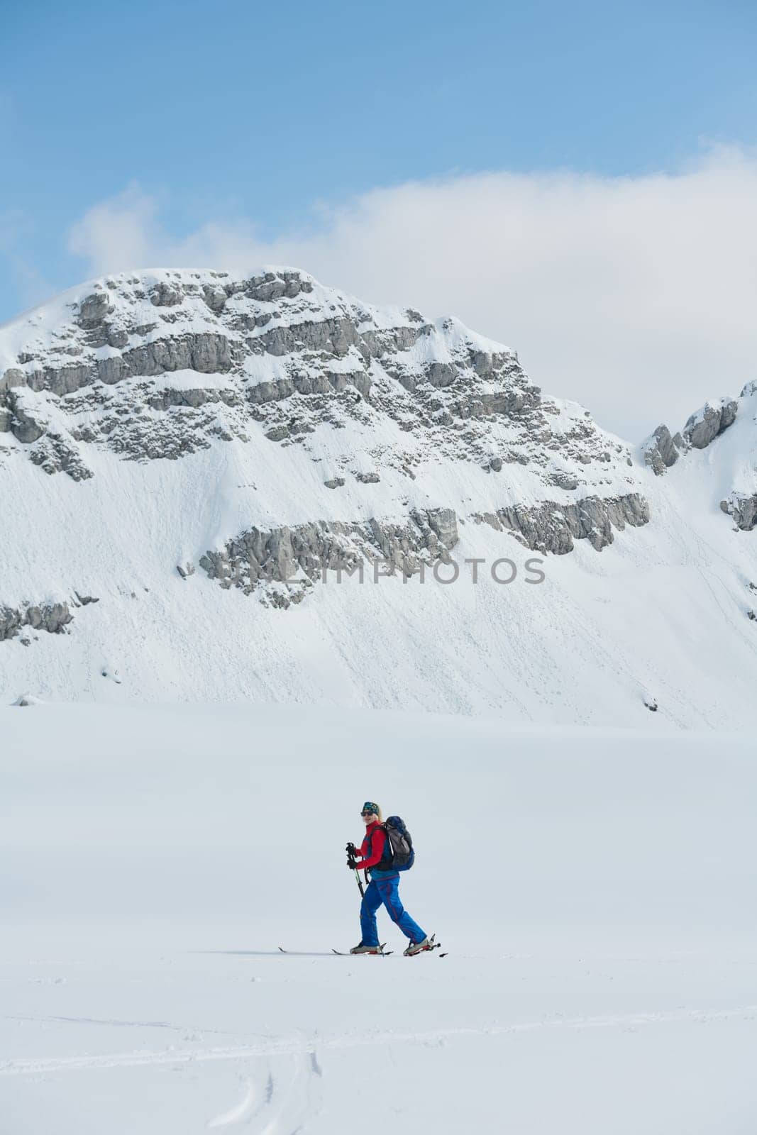 A female skier stands at the snowy summit of a mountain, equipped with professional gear and skis, poised for an exhilarating descent. by dotshock
