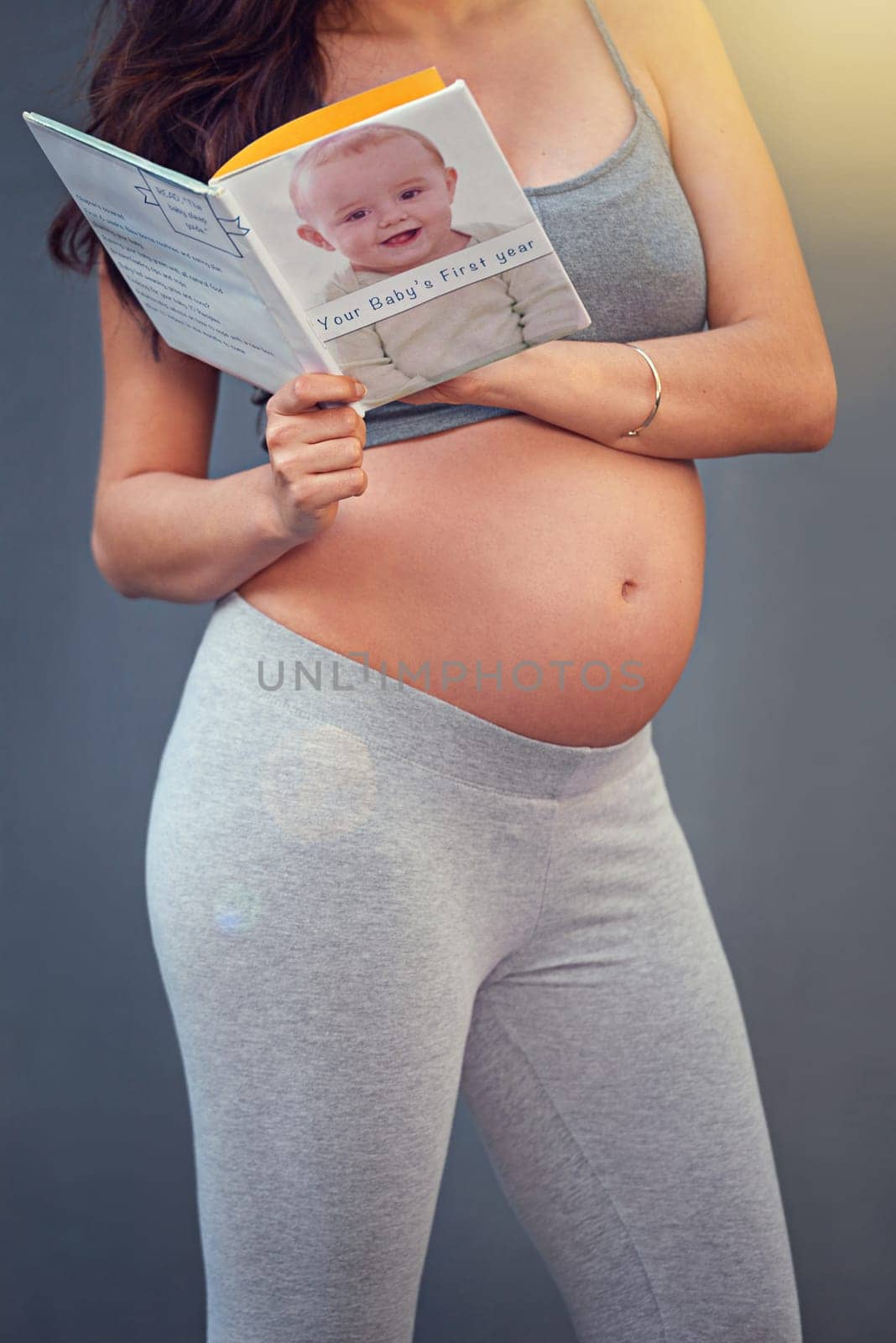 Pregnant woman, baby book and belly in studio for maternity and prenatal wellness for pregnancy and motherhood. Young person, happy and isolated with growing stomach or read for childbirth well being.