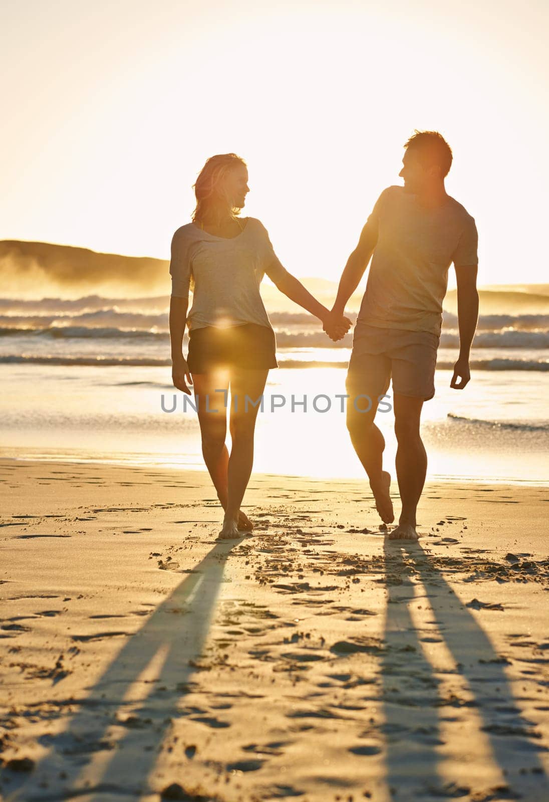 Lens flare, sunset and couple holding hands at beach, ocean and sea with affection, bonding and love. People, partners and romance for care together on vacation, holiday and travel in Australia by YuriArcurs