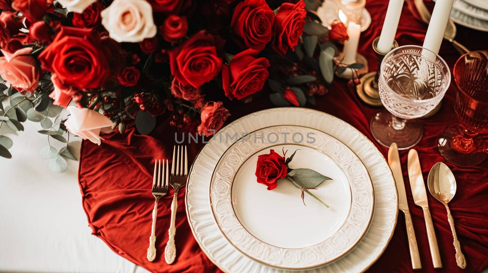 Festive table setting with cutlery, candles and beautiful red flowers in a vase.