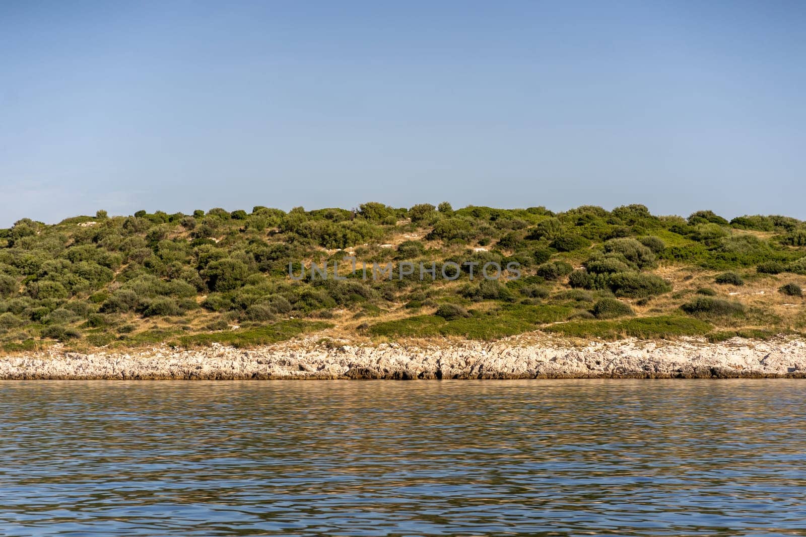 Strip of sea waves, rocky beach, grass and shrubs on hill of Dugi Otok island in Adriatic Sea, Croatia