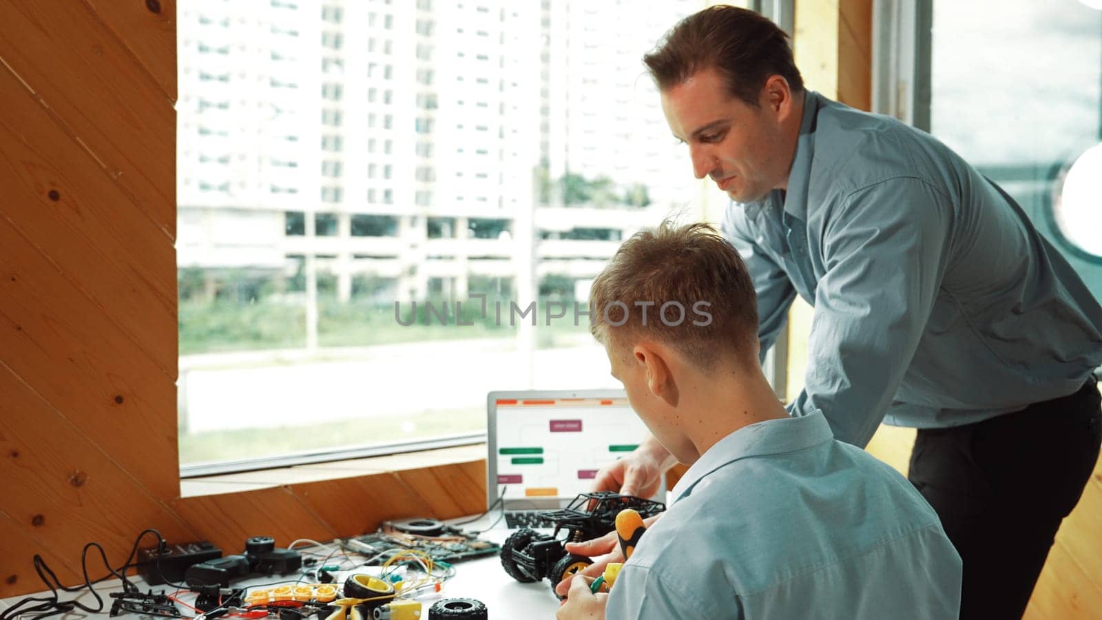 Caucasian teacher help student fixing car model and giving advise for programing system or coding prompt while highschool boy listen and use equipment to repair robot at STEM classroom. Edification.