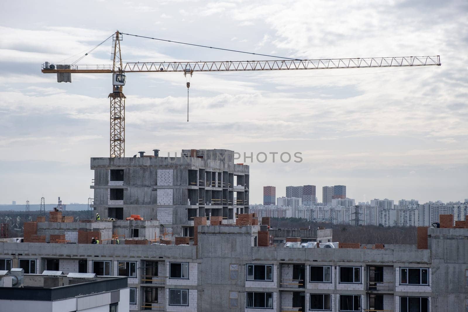 A crane and a building under construction against a blue sky background. Builders work on large construction sites, Building a house is not necessary for new high-rise buildings