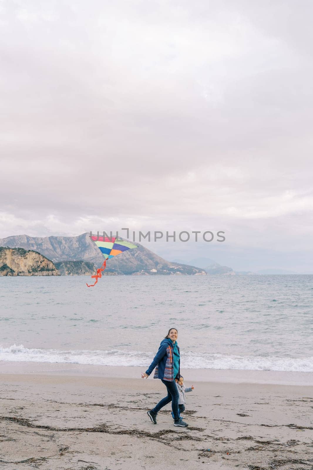 Mom with a little girl walk holding hands along the seashore with a kite on a string. High quality photo