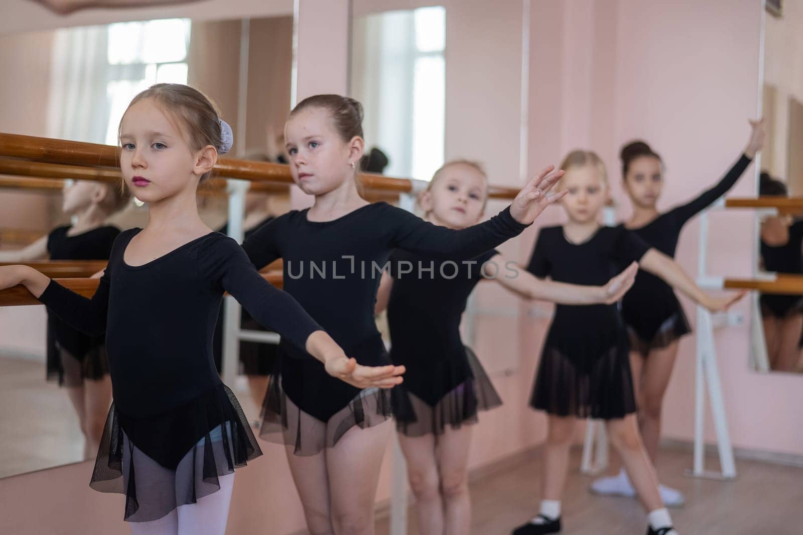 Cute little girls in black swimsuits and tutu do ballet at the barre