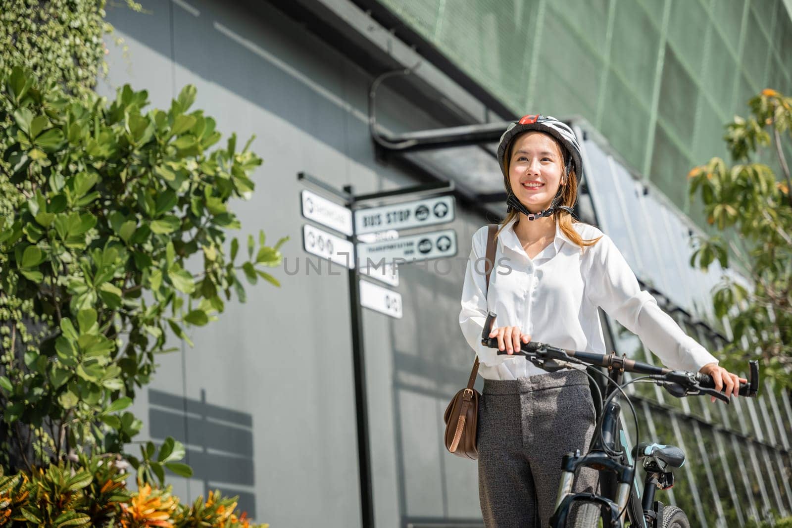 Asian businesswoman smiling by her bicycle suited up and helmeted is ready for her morning office commute. embodies modern concept of cheerful business commuter combining work and outdoor enjoyment.