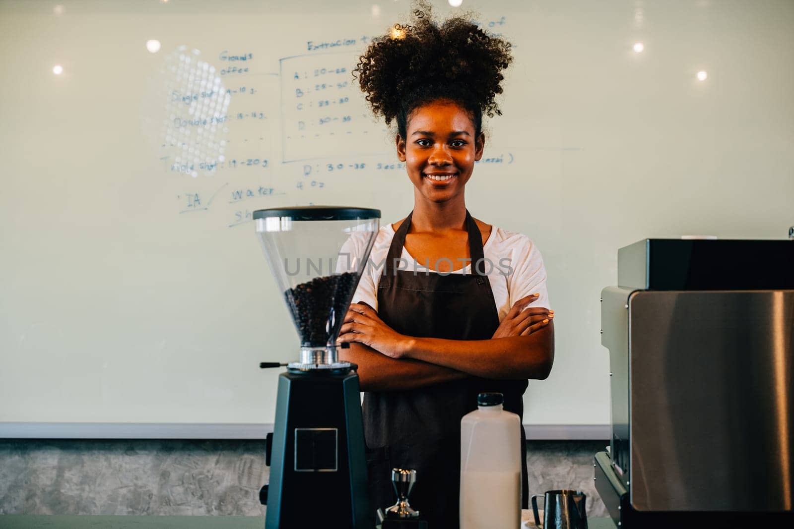 In the coffee shop confident black woman stands at the counter. Portrait of owner a successful businesswoman in uniform smiling with satisfaction providing great service. Inside a small business cafe by Sorapop