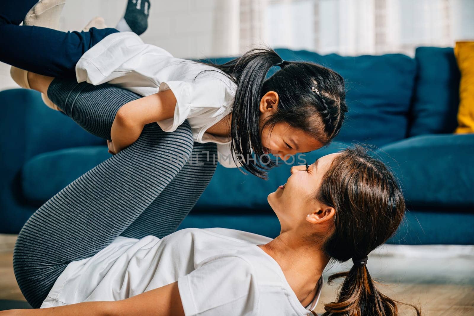 In a cozy setting a mother and her child practice family fitness imaginatively 'flying' like airplanes during their Pilates and yoga routine strengthening their bond and sharing happiness.