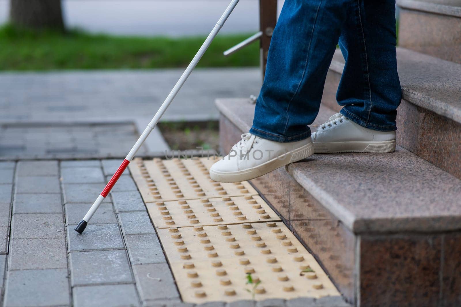 Close-up of female foot, walking stick and tactile tiles. Blind woman walking down stairs using a cane