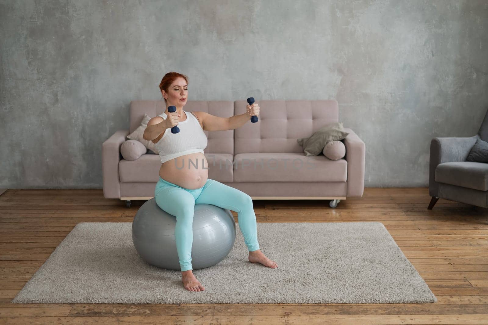 Pregnant woman doing exercises with dumbbells while sitting on a fitness ball at home. by mrwed54