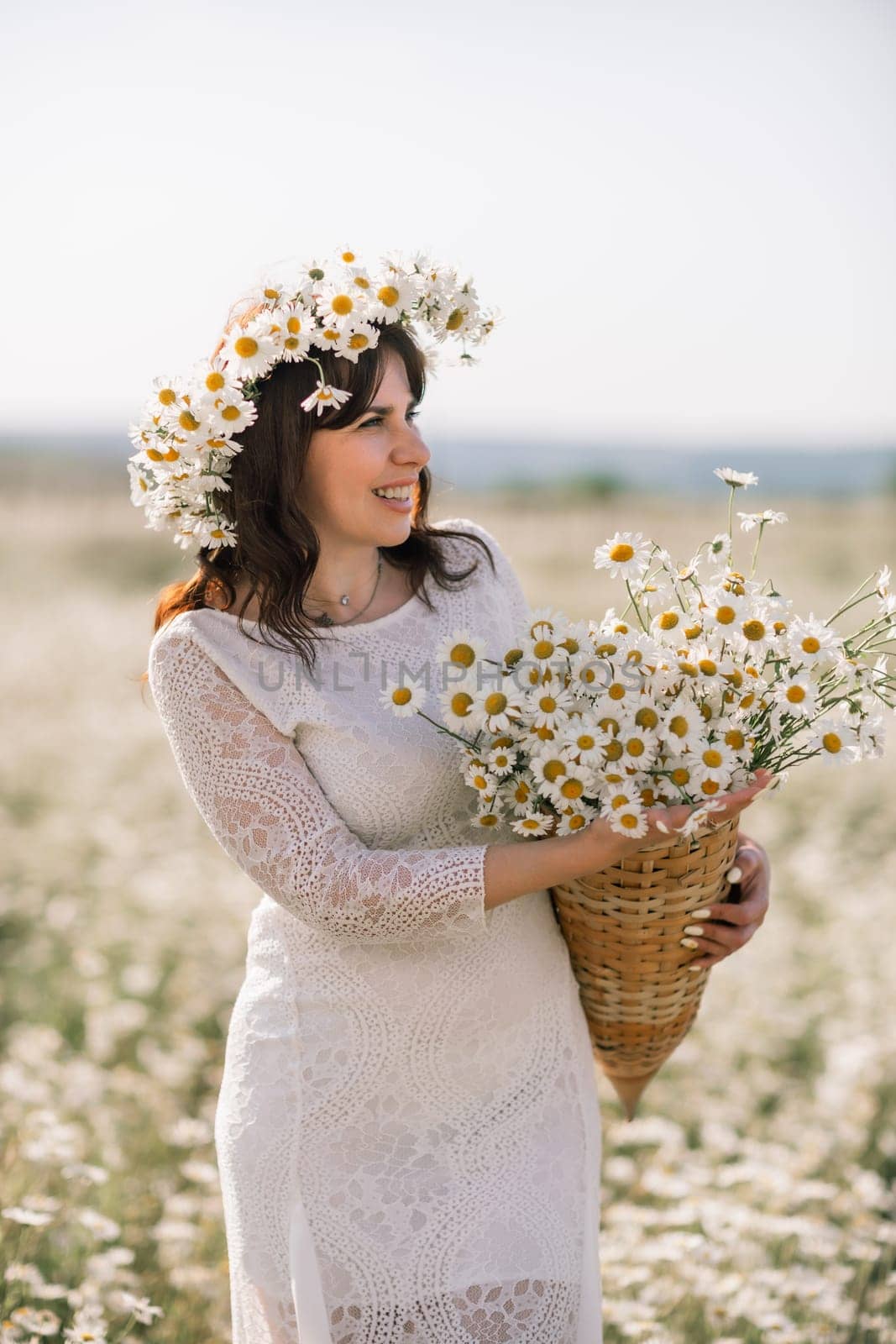 Happy woman in a field of daisies with a wreath of wildflowers on her head. woman in a white dress in a field of white flowers. Charming woman with a bouquet of daisies, tender summer photo by Matiunina