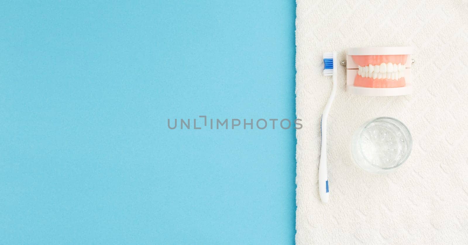 Toothbrush with glass of water and towel on blue background. Oral hygiene concept in the bathroom. Dentures on blue isolated background.