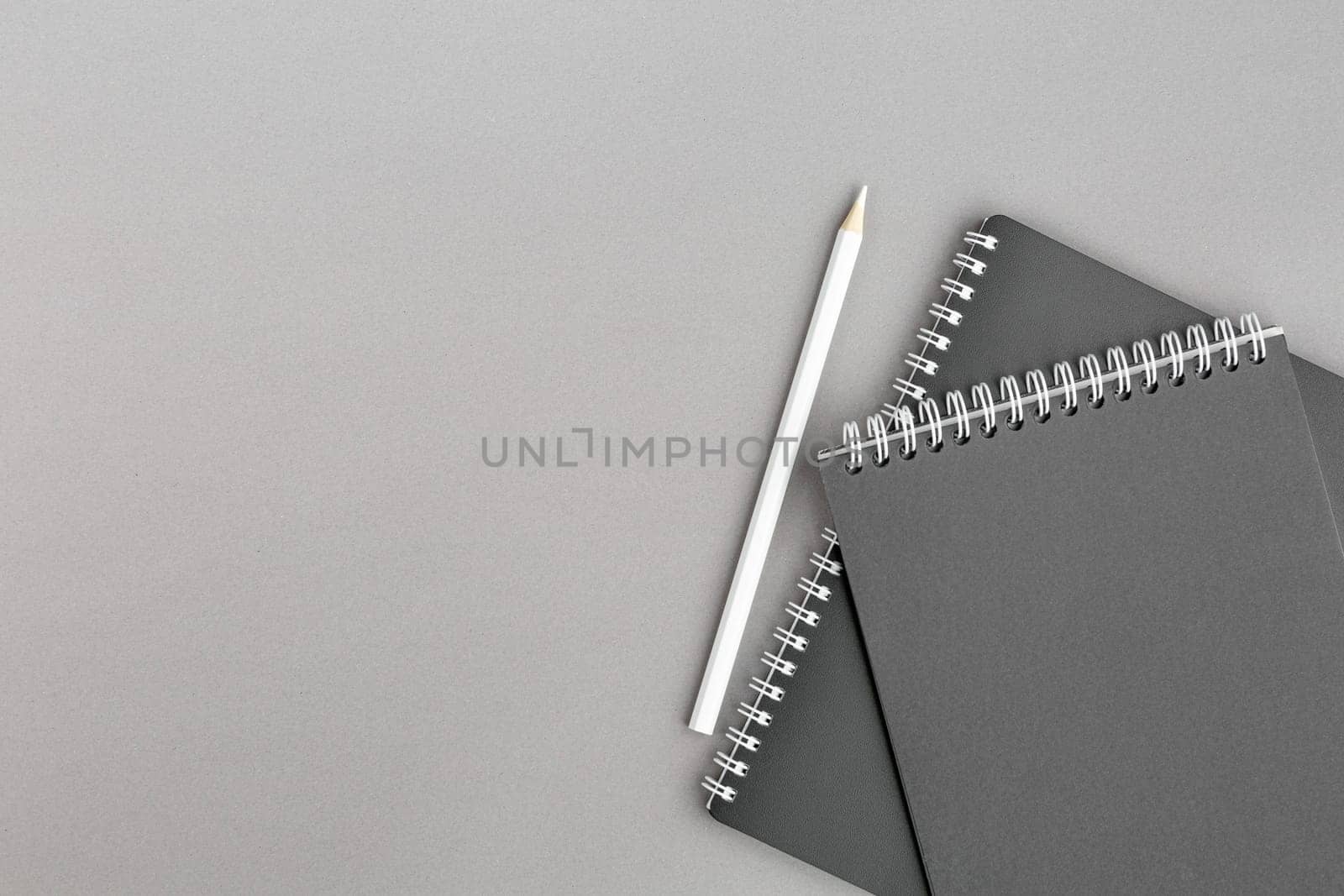 Spiral notebook with black paper sheets and white pencile on gray isolated background. Top view close up.