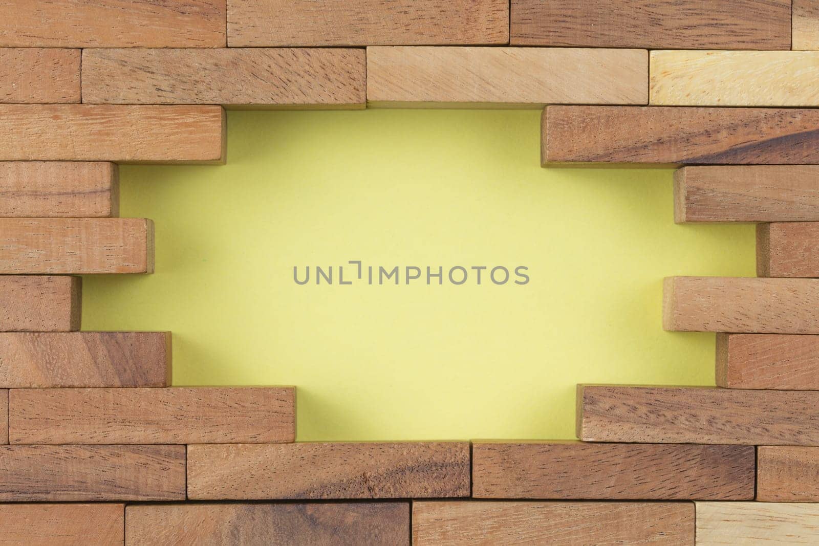 Wooden blocks laid out in the form of a brick wall with a hole in the middle on a yellow background. Top view.