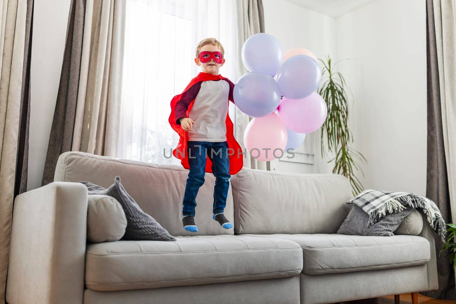 Child in superhero costume with balloons. Home celebration photography with copy space. Birthday party concept. Design for invitation, banner