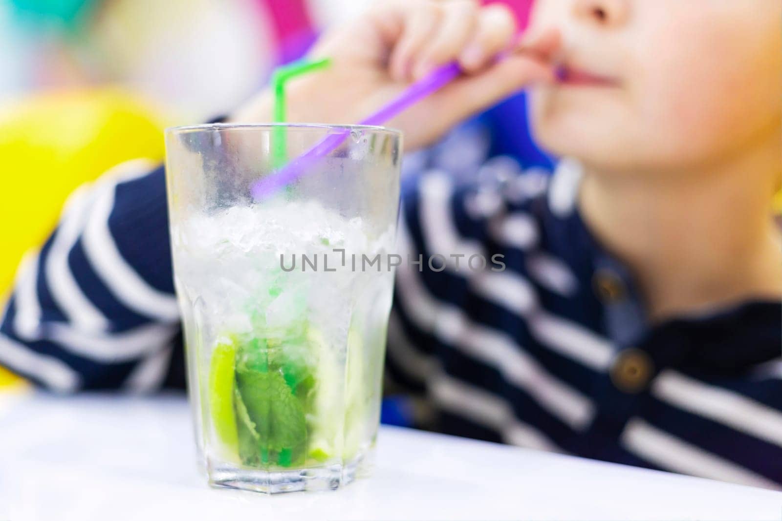 Child sipping lemonade from glass with straw. by andreyz