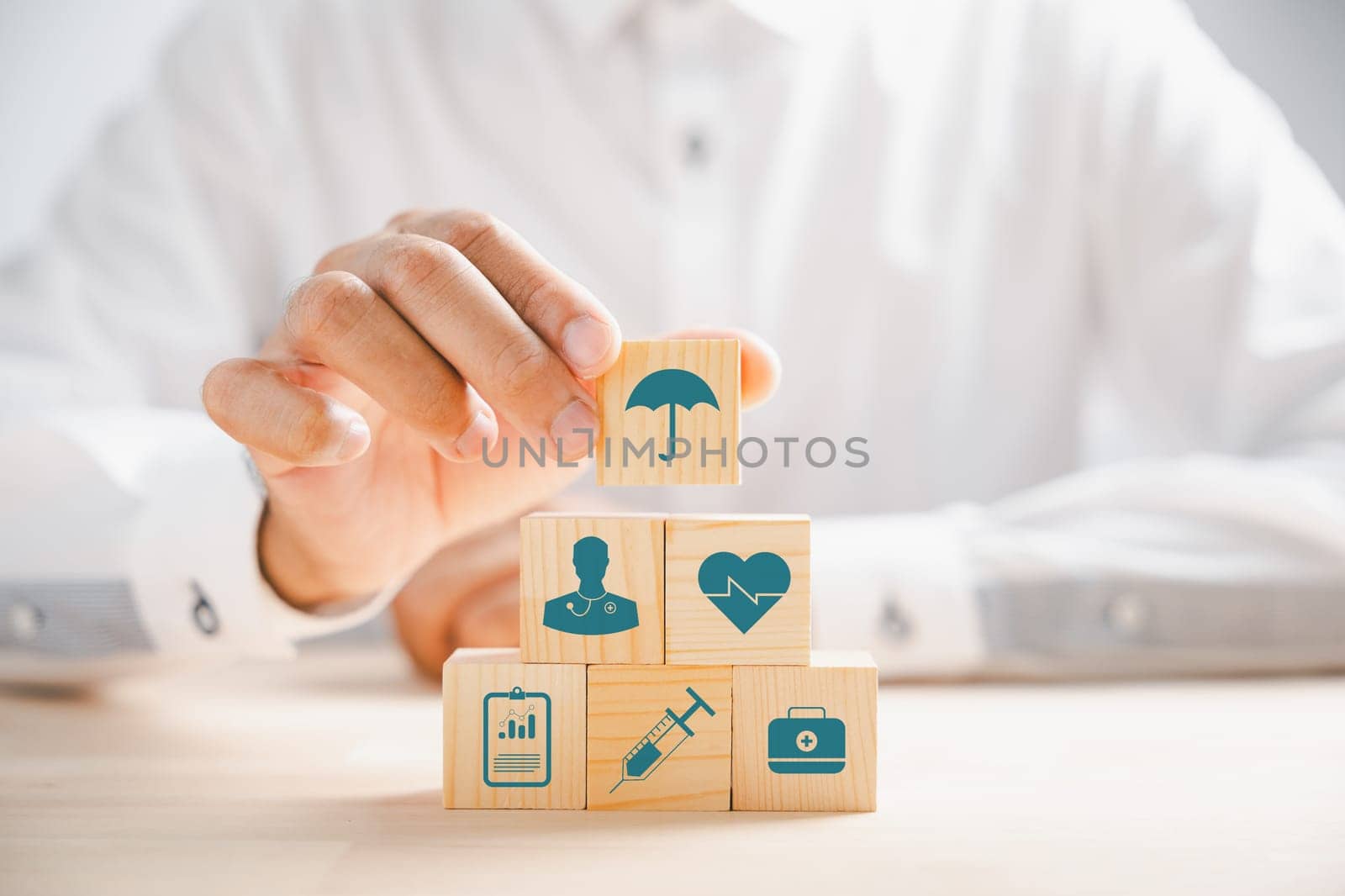 Hand holding a wooden block adorned with healthcare and medical icons. Depicting safety and health, symbolizing pharmacy, family care, and heart well-being. A concept of happiness.