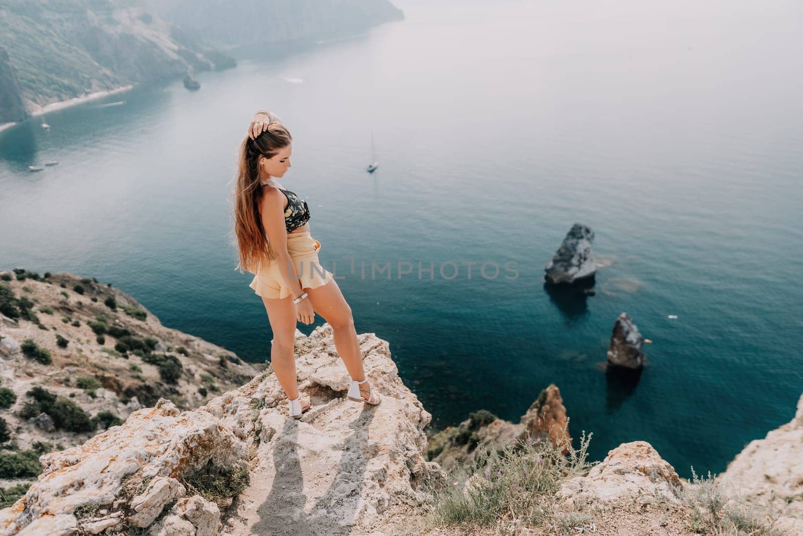 Woman travel sea. Happy tourist taking picture outdoors for memories. Woman traveler looks at the edge of the cliff on the sea bay of mountains, sharing travel adventure journey.