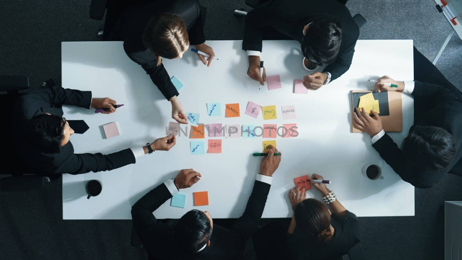 Top down aerial view of diverse business people writing marketing idea or taking a note on sticky notes. Professional executive manager group brainstorm financial plan at meeting room. Directorate.