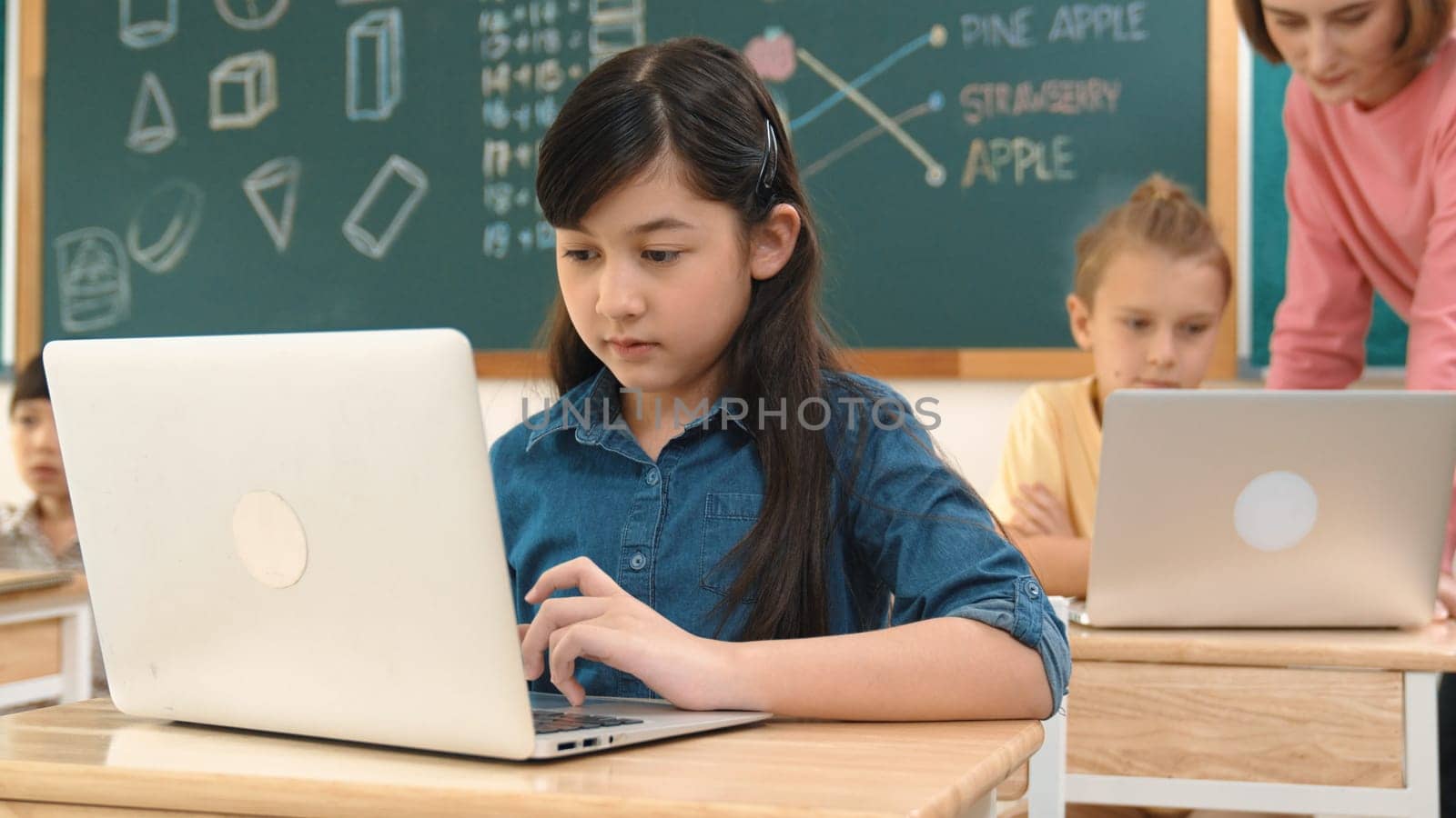 Cute girl looking at laptop screen while coding engineering prompt. Multicultural student learning about generated AI while teacher teaching about system or checking classwork at STEM class. Pedagogy.