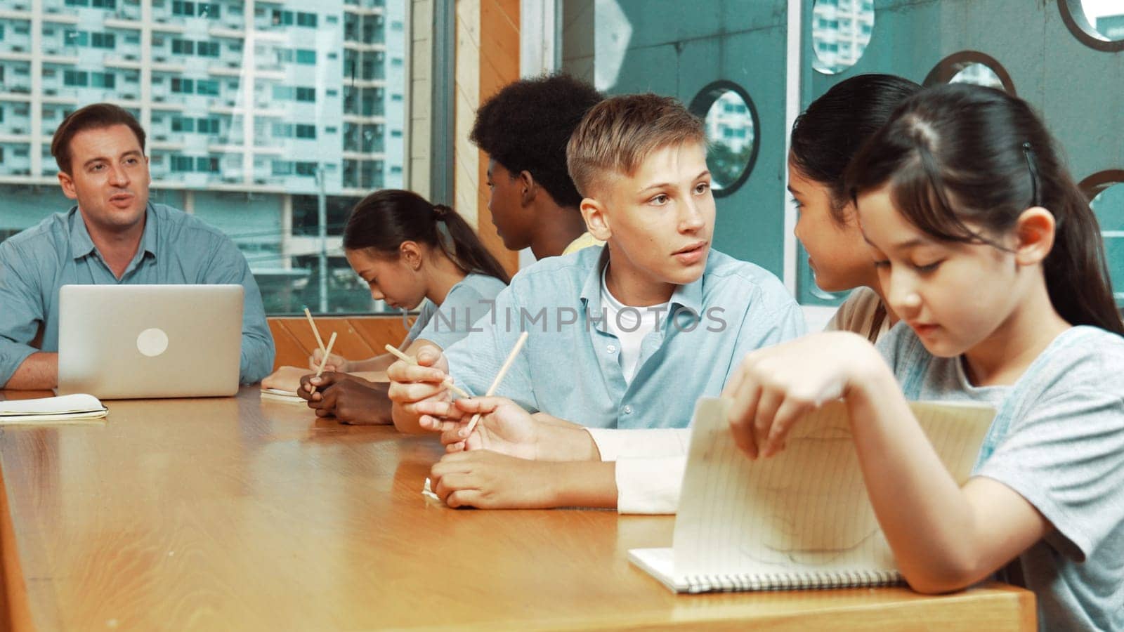 Caucasian teacher and multicultural students clapping hand or putting the hand in the air together to celebrate for successful project with laptop and equipment placed on table in class. Edification.