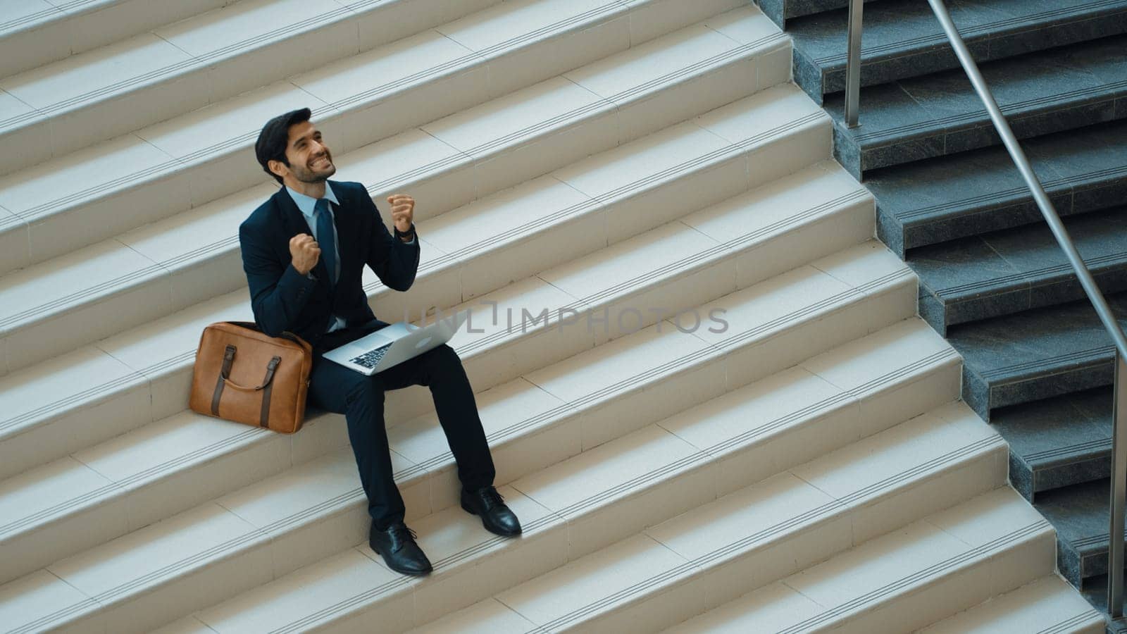 Top view business man celebrate successful project while sitting at stairs. Smart project manager getting new gob, getting promotion, increasing sales while calling friends by using laptop. Exultant.