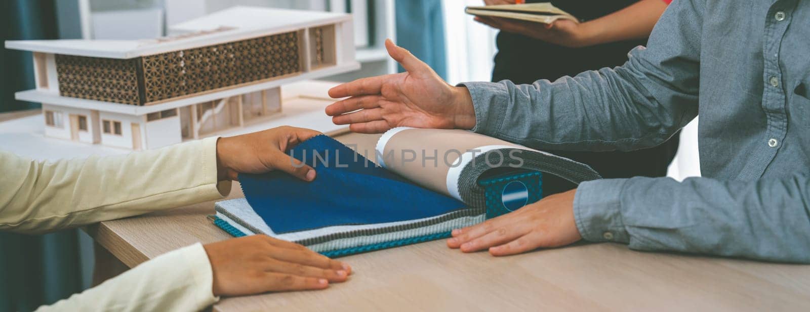 Skilled interior designer presents curtain material during customer selects material carefully with house model placed on table at modern office. Creative working and design concept. Variegated.
