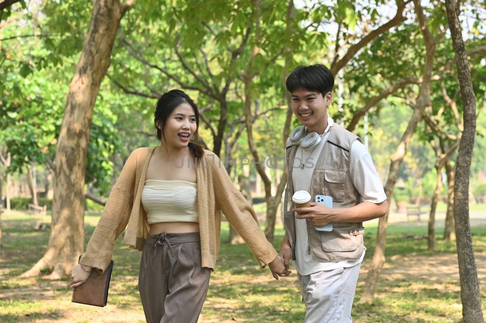 Portrait of a cheerful young couple in Love holding hands and walking in summer green park.
