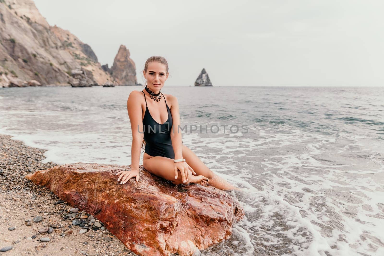 Side view a Young beautiful sensual woman in a mint long dress posing on a volcanic rock high above the sea during sunset. Girl on the nature on overcast sky background. Fashion photo