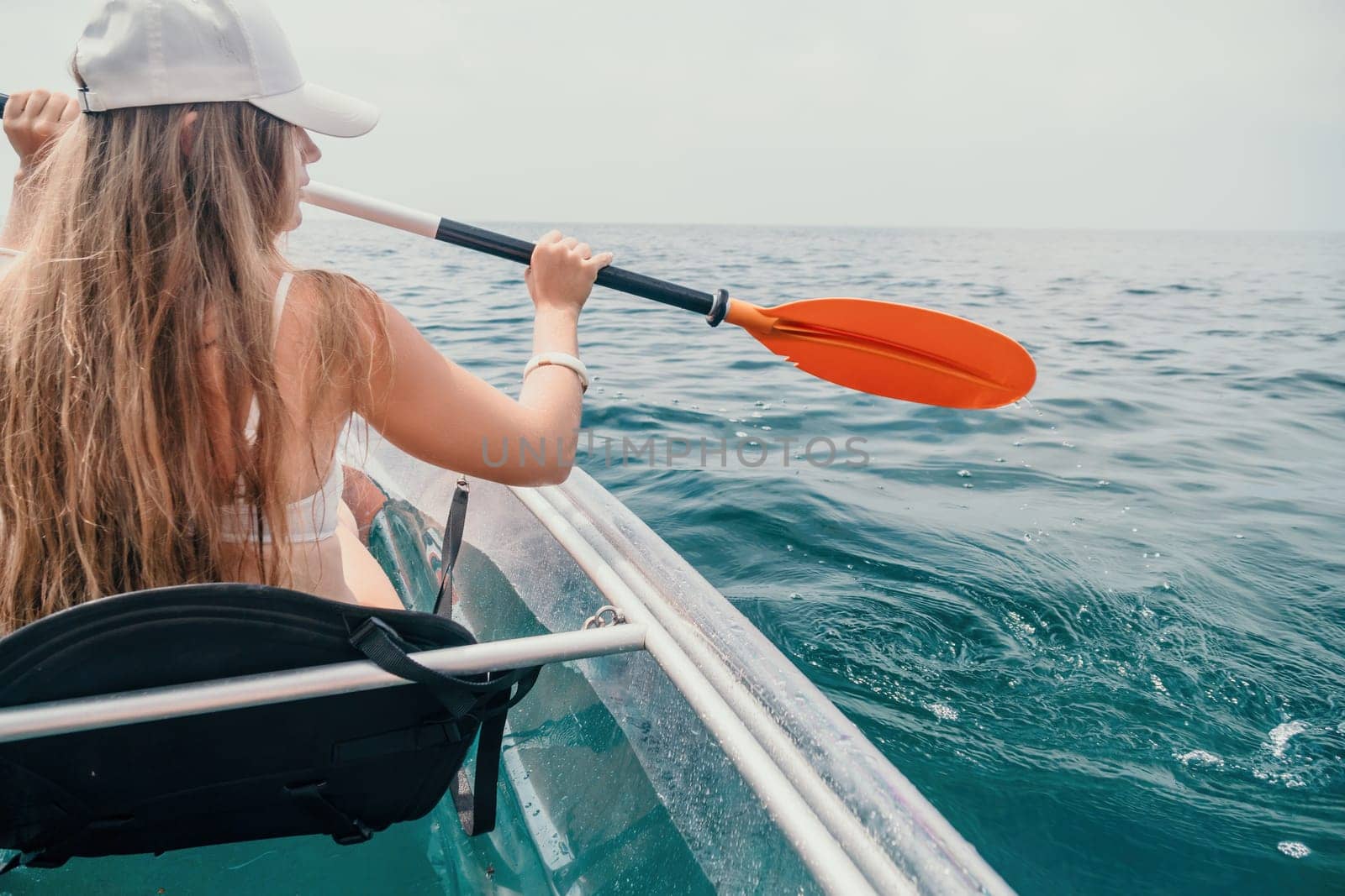 Woman in kayak back view. Happy young woman with long hair floating in transparent kayak on the crystal clear sea. Summer holiday vacation and cheerful female people having fun on the boat.