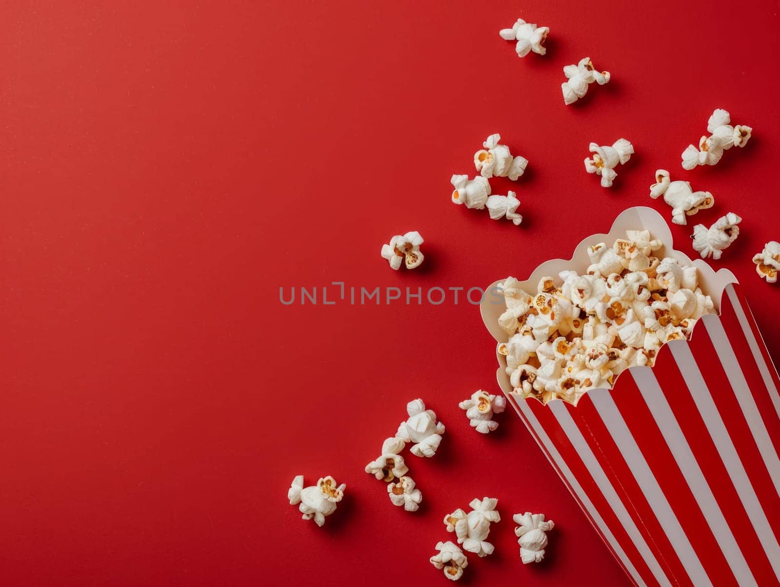 Popcorn is scattered from a striped box isolated on a red background. Top view with copy space. Movies leisure time by papatonic