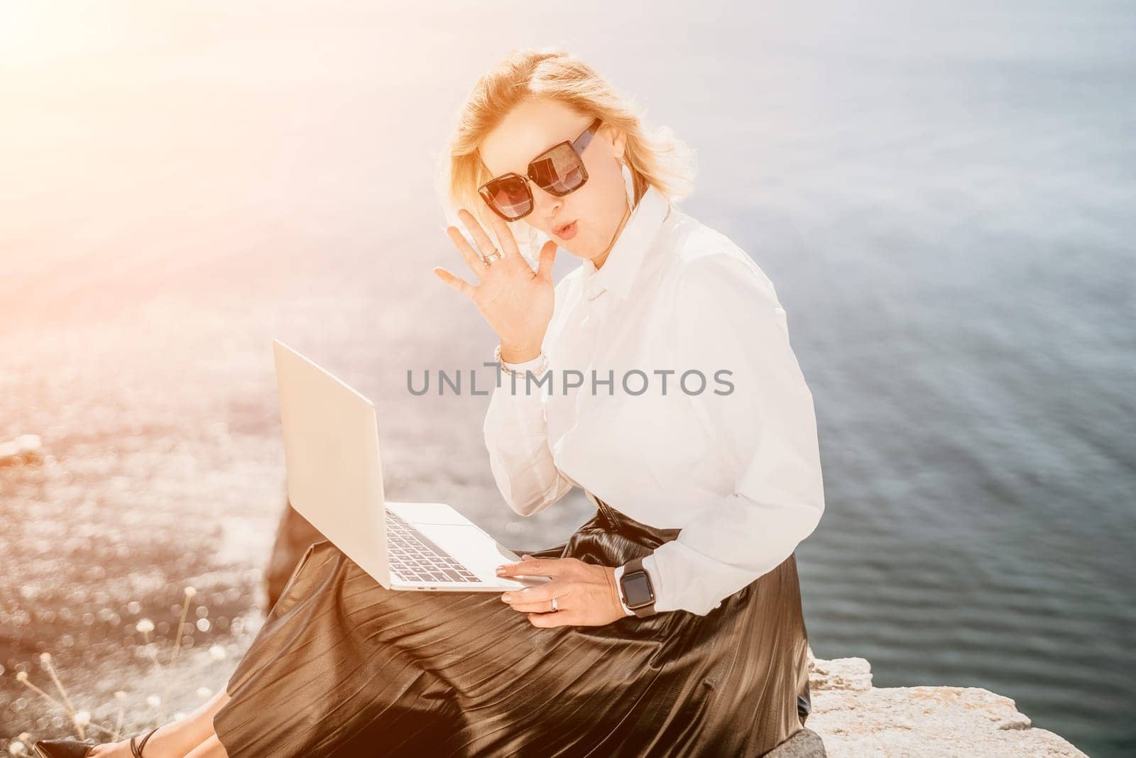 Digital nomad, Business woman working on laptop by the sea. Pretty lady typing on computer by the sea at sunset, makes a business transaction online from a distance. Freelance, remote work on vacation